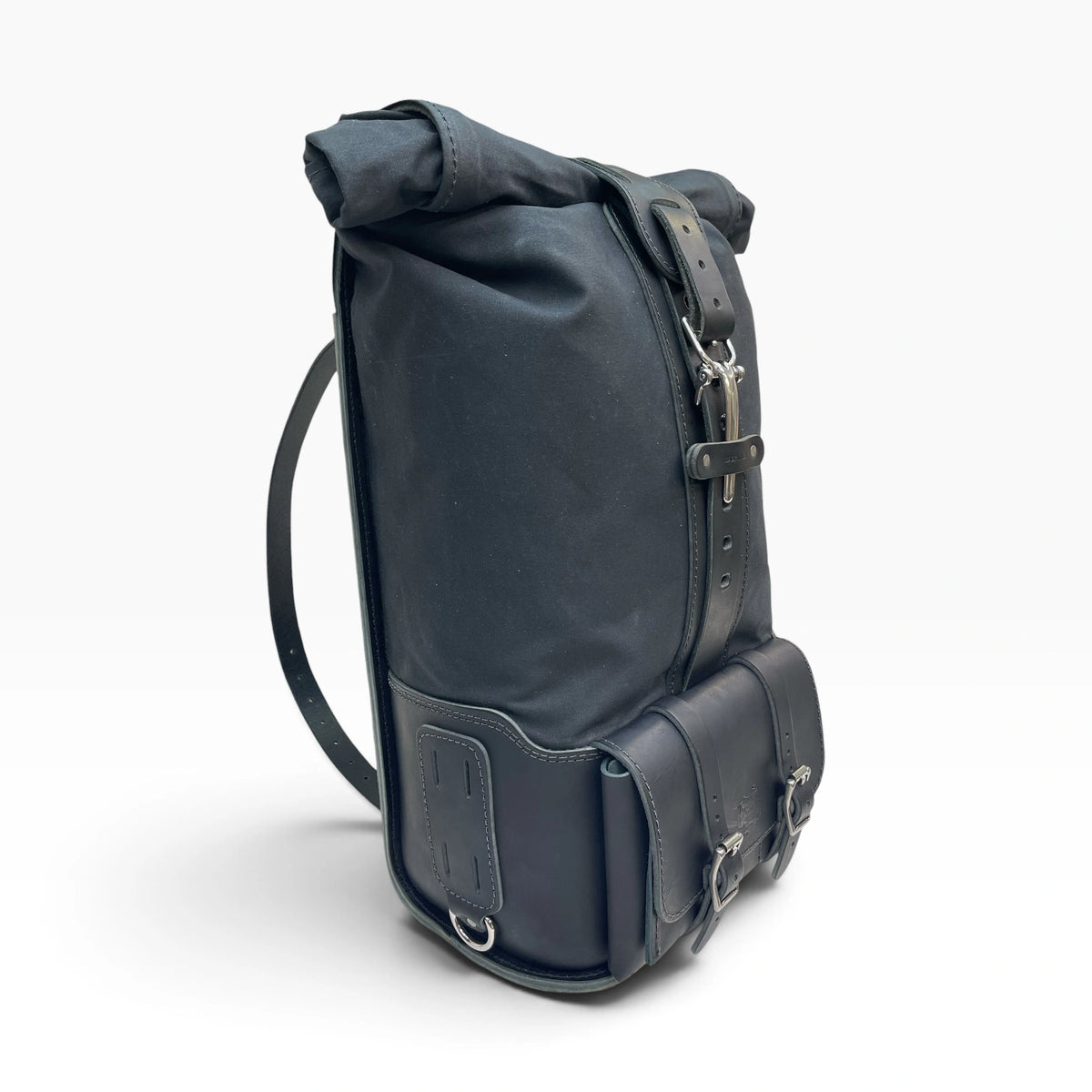 A black roll-top backpack with leather straps, buckles, and a front utility pocket, shown from a three-quarter angle on a light gray background.