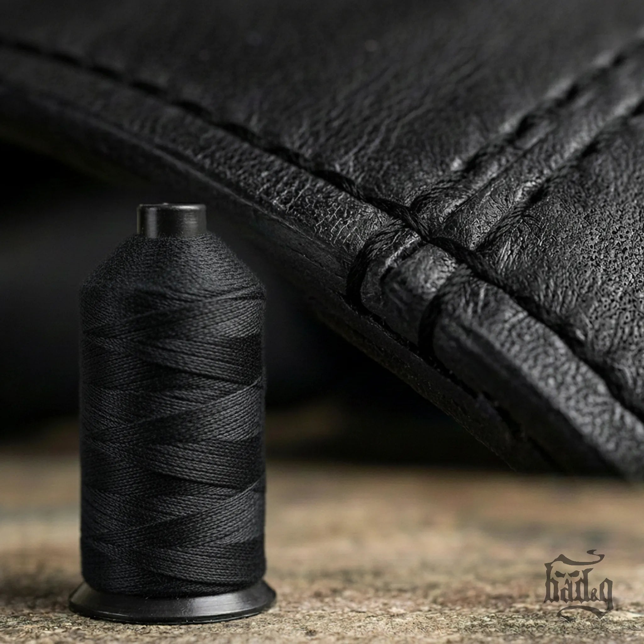 Spool of black thread next to a piece of black leather